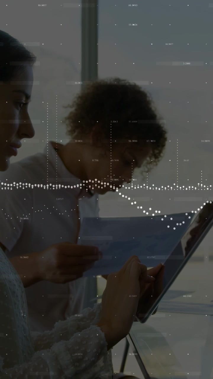 Vertical video: Two men tapping tablet and reading paper at desk, business waveform showing data