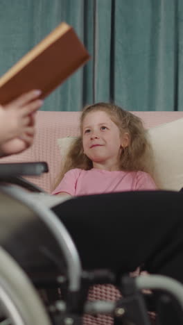 adorable sister and brother listen to mom reading funny tale smiling. woman with leg injury sits in wheelchair spending time with children closeup