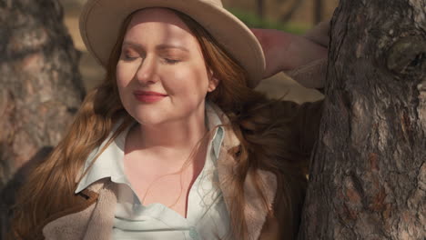 portrait of a attractive smily red haired woman wearing a camel hat in the forest