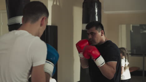 friendly sparring of professional boxers in gym. young sportsman exercises with instructor in public fighting club slow motion. physical activity