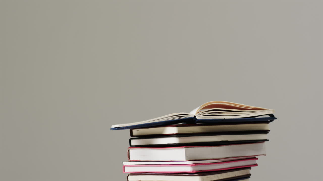 primer plano de un libro abierto en una pila de libros sobre un fondo gris, en cámara lenta
