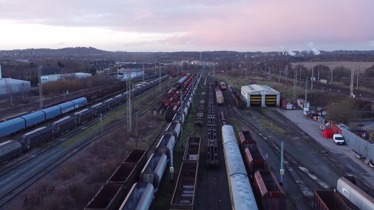 Sunrise aerial view of long railroad tracks with heavy diesel locomotive carriages and cargo container yard rising forwards