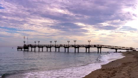 Lapso-De-Tiempo-De-4k-De-Un-Muelle-De-Madera-En-La-Playa-De-Marbella-En-La-Milla-De-Oro-Al-Atardecer,-Hermosa-Vista-Escénica-De-Vacaciones-De-La-Costa-Del-Sol