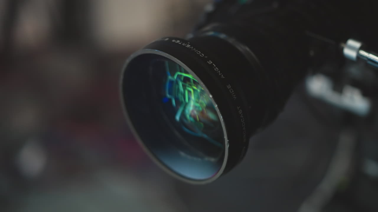 Close up high end camera lens reflecting green and blue studio lights, showcasing glass elements, focus rings, lens coatings. Highlighting technical optics detail for creative filmmaking