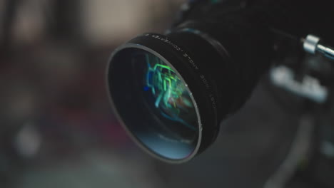 close up high end camera lens reflecting green and blue studio lights, showcasing glass elements, focus rings, lens coatings. highlighting technical optics detail for creative filmmaking