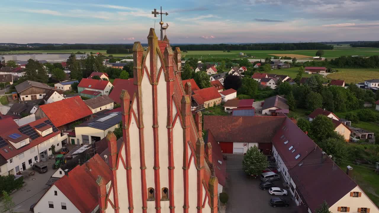 A stork perched on a church steeple in a small rural town at sunset, aerial view