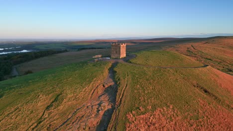 Squat-stone-tower-on-hilltop-with-pull-away-revealing-hillside-lit-by-dawn-sunshine-with-pathways