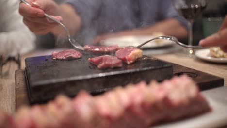 friends eating at restaurant celebrating birthday in dinning room, toasts, cheers and preparing their own meat at hot stone