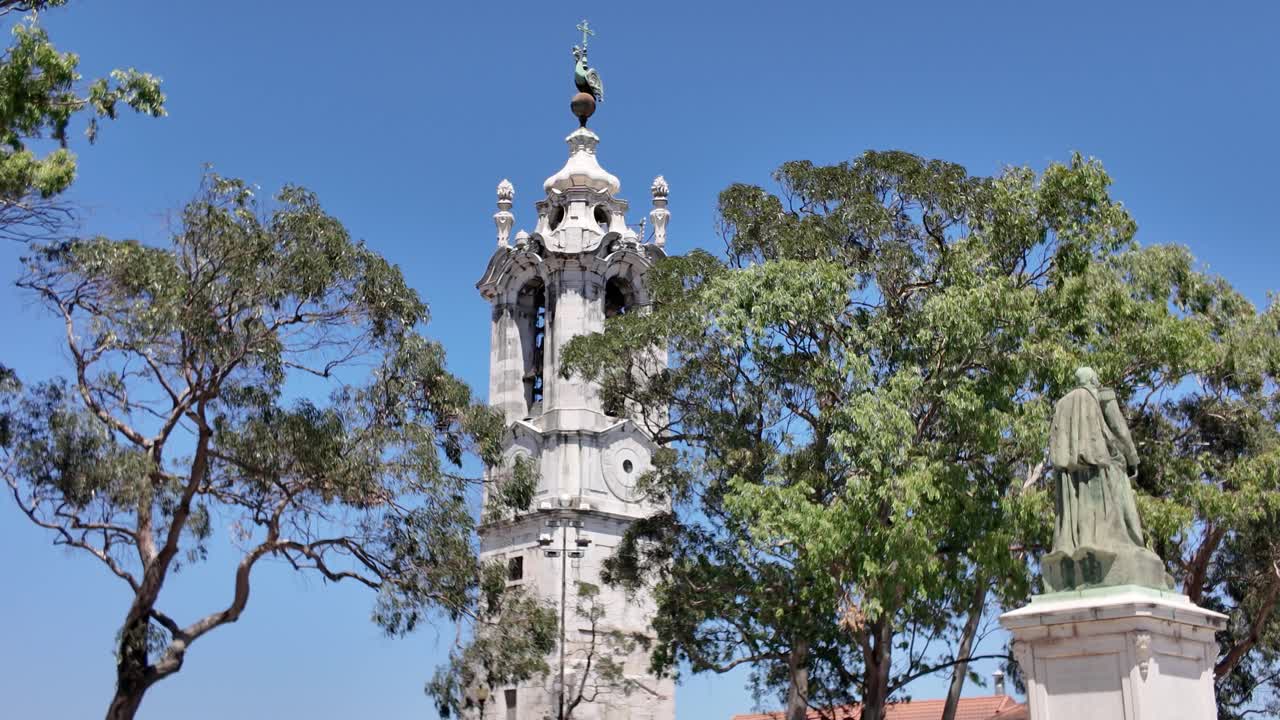 Statue and Torre Paroquial tower under clear blue sky in Lisbon Portugal with surrounding trees