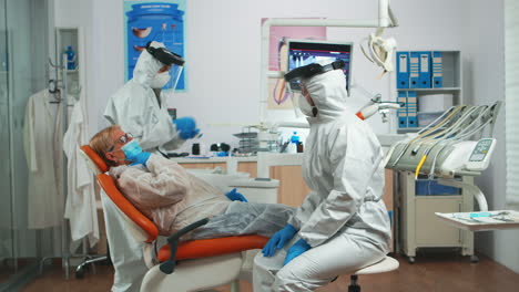 mujer explicando el problema dental al médico usando un traje de protección