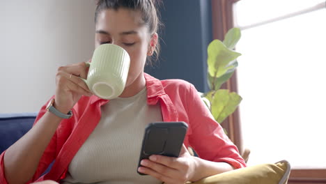 Adolescente-Birracial-Enfocada-Bebiendo-Té-Y-Usando-Un-Teléfono-Inteligente-En-Casa,-Copiando-Espacio,-Cámara-Lenta