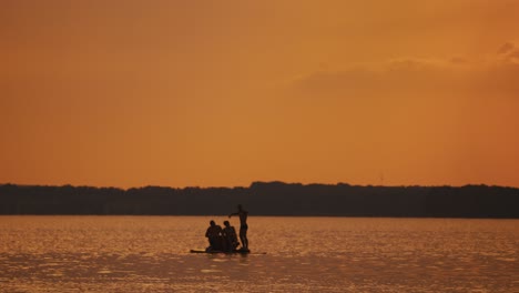 happy men have good time in catamaran at orange sunset. three young guys rafting in catamaran along the river on water in the evening.