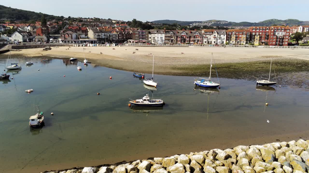 Vista aerea di barche in bassa marea luccicante, soleggiato e caldo, nel porto turistico sulla spiaggia di sabbia di Rhos-on-Sea, con orbita a sinistra