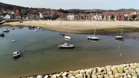 Aerial-view-boats-in-shimmering-low-tide-sunny-warm-Rhos-on-Sea-seaside-sand-beach-harbour-resort-orbit-left