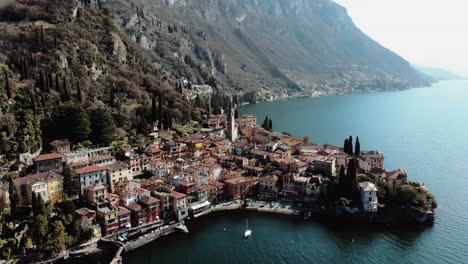 Vista-Aérea-De-Drones-Cerrando-Casas-Junto-A-Un-Lago-En-Los-Alpes,-Pequeña-Ciudad-Idílica-Y-Tranquila-Cerca-De-La-Superficie-Del-Agua