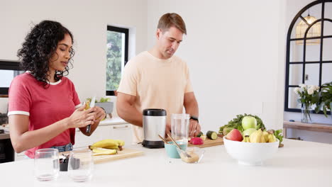 preparing healthy smoothie, young multiracial couple cutting fruits and vegetables, at home