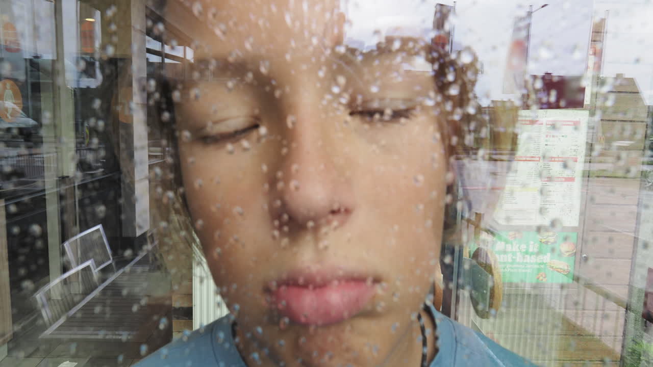 어린 소년은 비가 흐르는 창문을 통해 쳐다본다.