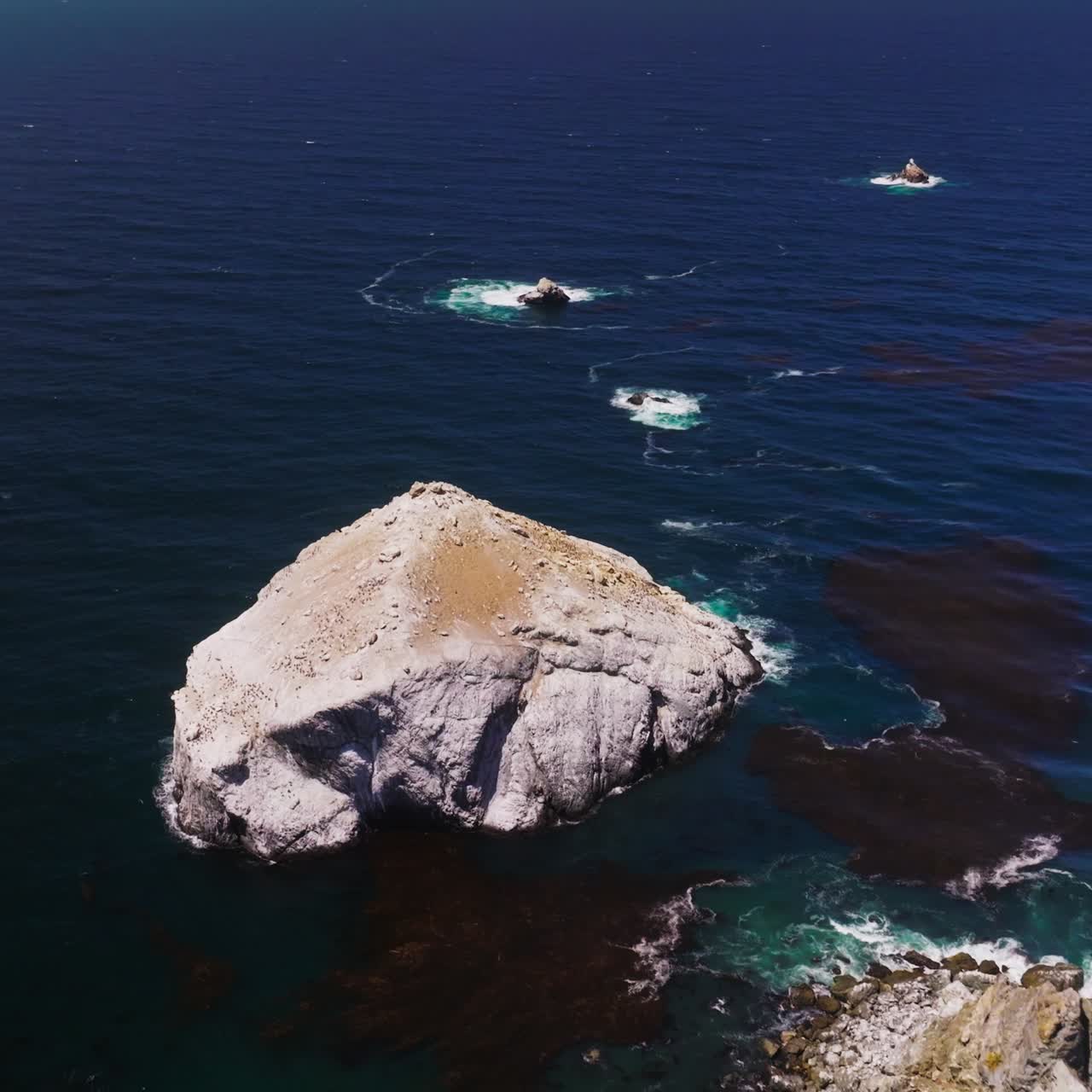 Bare rocks of different size peeping out from deep blue water. Pacific ocean at the coastline of California, USA from top