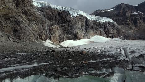 Gran-Glaciar-En-Los-Alpes-Italianos-Con-Cueva,-Lago-Verde-Glacial-Y-Roca-Sobre-El-Hielo,-Toma-Aérea-De-Abajo-Hacia-Arriba