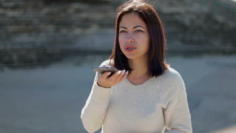 serious young woman talking through loudspeaker in smartphone