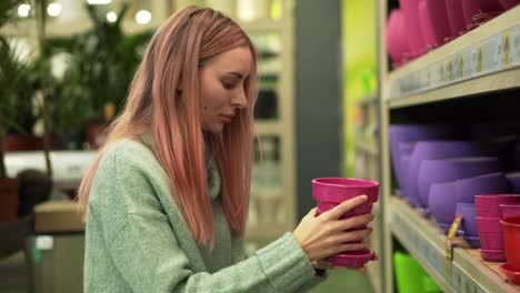 woman choosing colorful pot for home plants from shelves of a flower shop