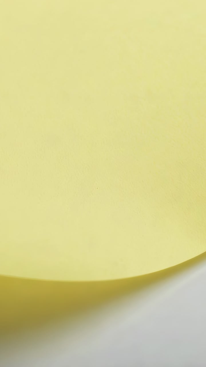 Vertical video: Shifting camera revealing pale yellow sheet on white tabletop, showing curved edge