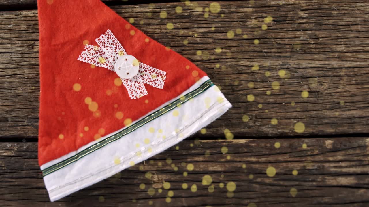 All'inizio, cappello di Babbo Natale rosso che scivola verso l'alto, ruotando su un tavolo, con scintillii che fluttuano per una rivelazione festiva