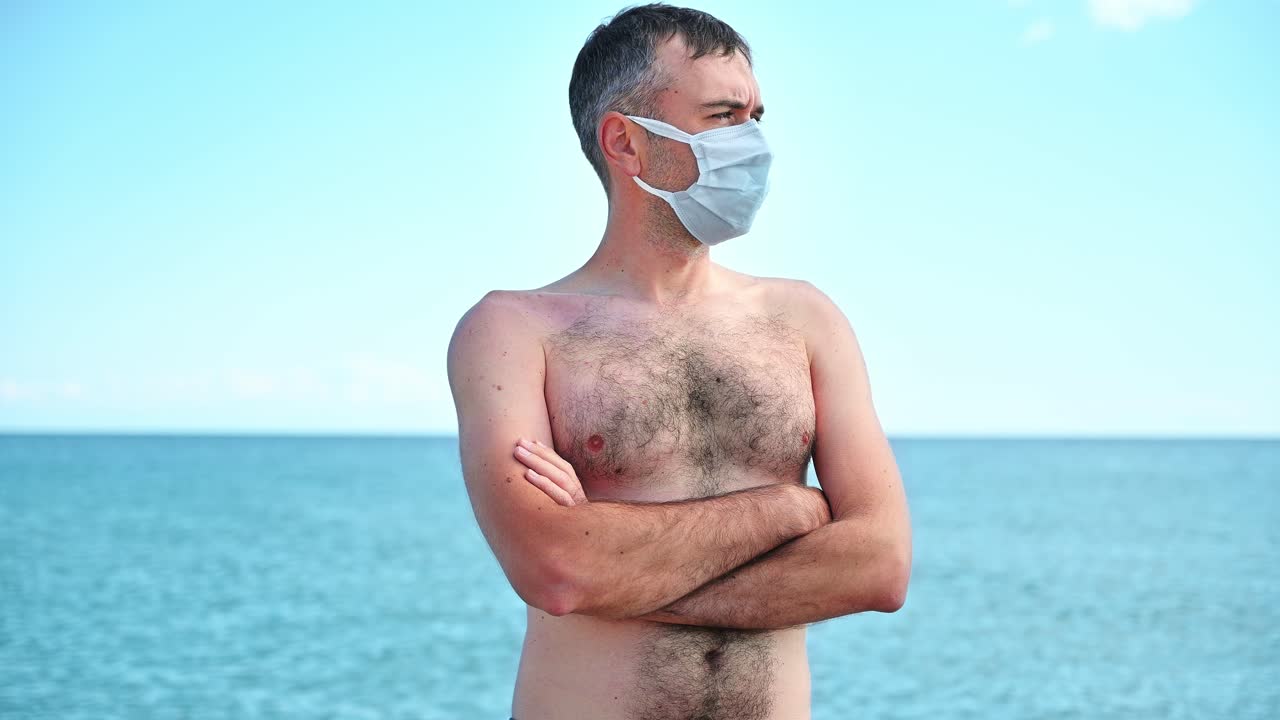 Portrait of a man in white medical mask on the Aegean sea shore in Greece, water on the background