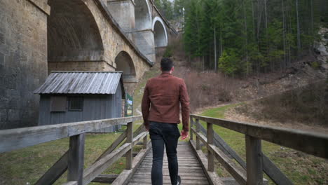 a man walks across a wooden bridge next to a rail viaduct - train bridge over a valley - semmering bahn - unesco world heritage - "kalte rinne