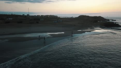surfers running with a surfboard towards the ocean during sunset in peru
