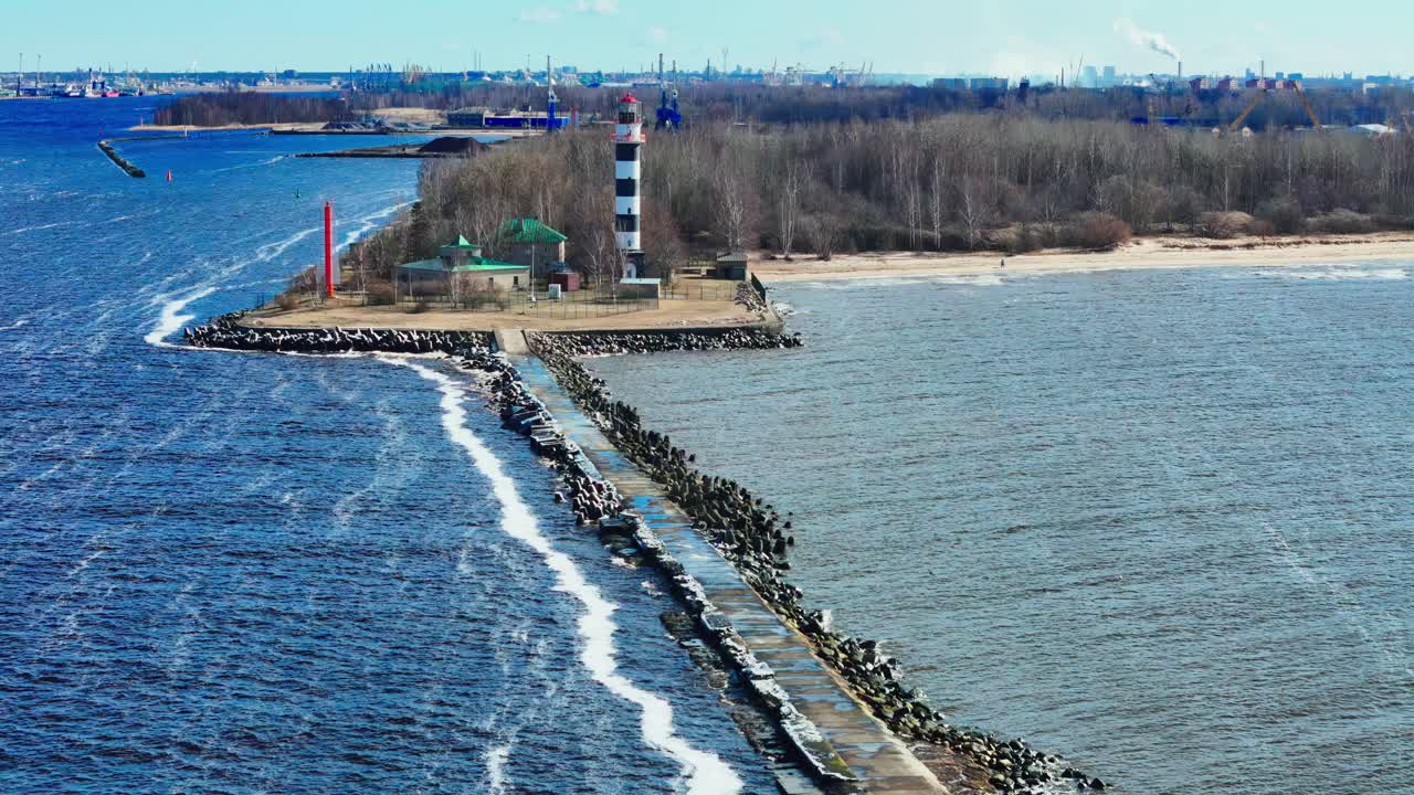 Aerial shot of a lighthouse on a pier located at a river mouth meeting the sea, Latvia