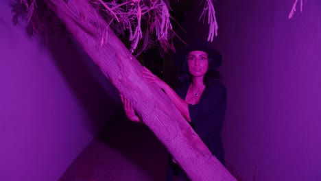hermosa mujer posando cerca de un árbol con luz púrpura y camina hacia el callejón - plano medio