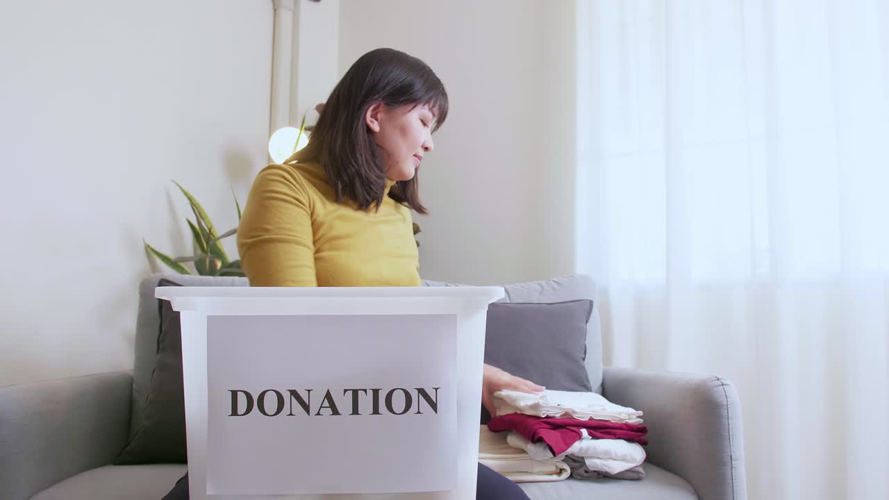 Portrait of Woman selecting clothes for donation and putting in box