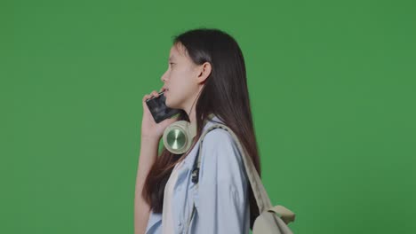 녹색 화면 배경 스튜디오에서 는 동안 스마트폰으로 이야기하는 배을 가진 아시아 십대 소녀 학생