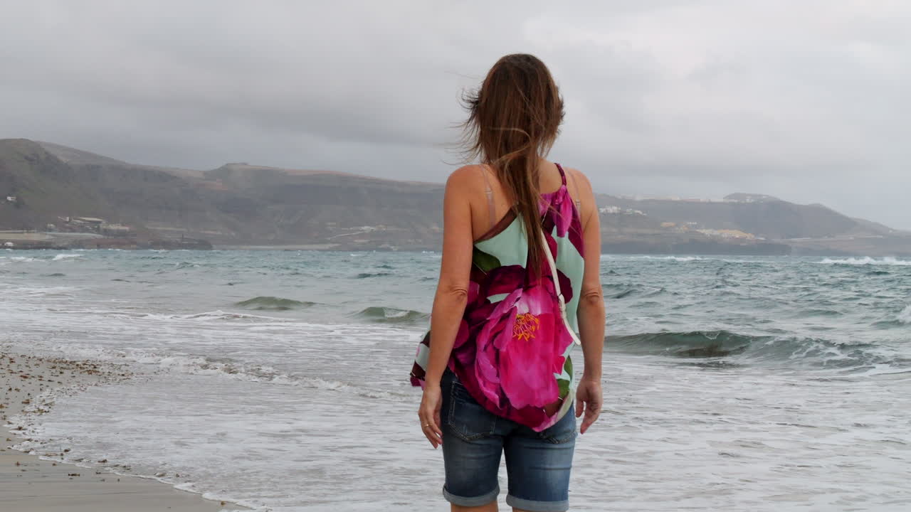 toma cinematográfica al amanecer de una mujer caminando por la orilla de la playa de las canteras