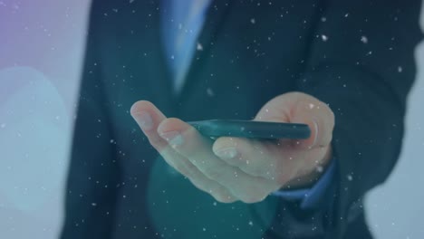 Animation-of-snow-falling-and-light-spots-over-caucasian-businessman-using-smartphone