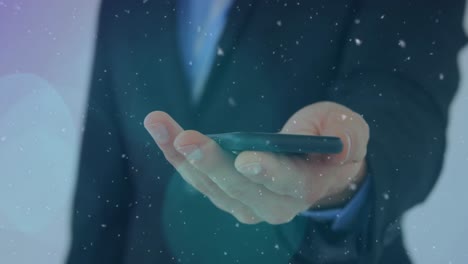 animation of snow falling and light spots over caucasian businessman using smartphone