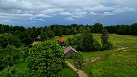 View-on-a-calm-rural-family-house-with-a-nice-green-garden,-a-small-lake-and-green-fields-around-on-a-cloudy-day,-slow-motion-with-copy-space,-aerial-drone-flight