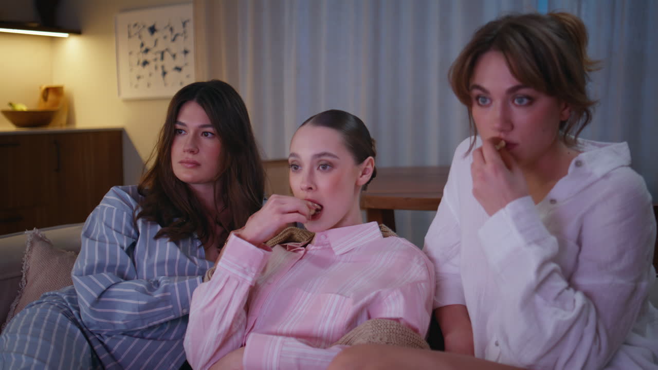 Girls scared horror movie on night home couch closeup. Women watching scary film