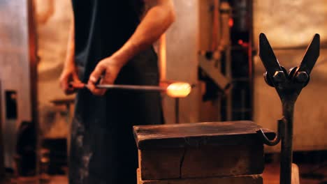 mid section of glassblower shaping a molten glass