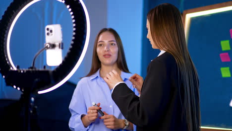 two brunette ladies talk actively to each other and turn to camera with light ring. blogging concept. streaming online.