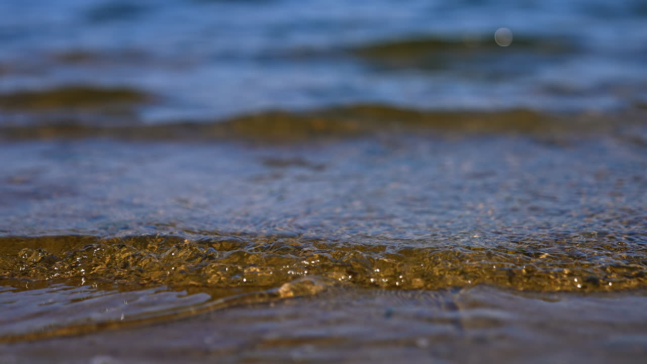 Slow waves come up to the sandy shore. Close up view on the river bank on sunny day.