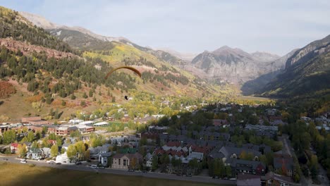 a rotating drone shot, of a paraglider flying over a neighborhood in the town of telluride, colorado, on a sunny day in the fall season