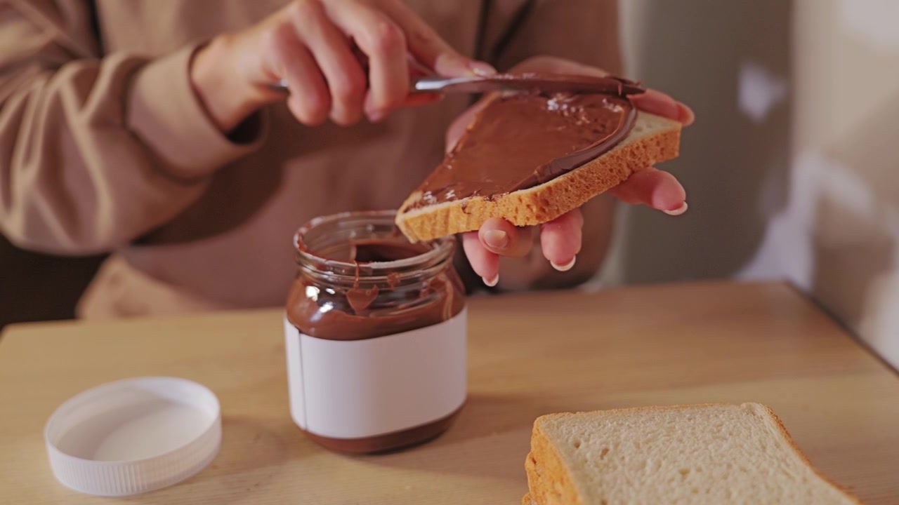 Un primo piano mostra un coltello che spalma uniformemente crema dolce alle nocciole per una gustosa colazione.