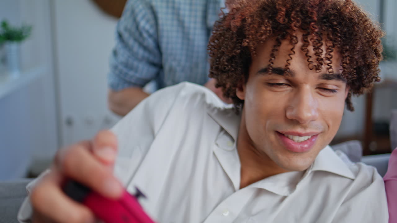 Curly teenager playing video game with friends at home closeup. Young players