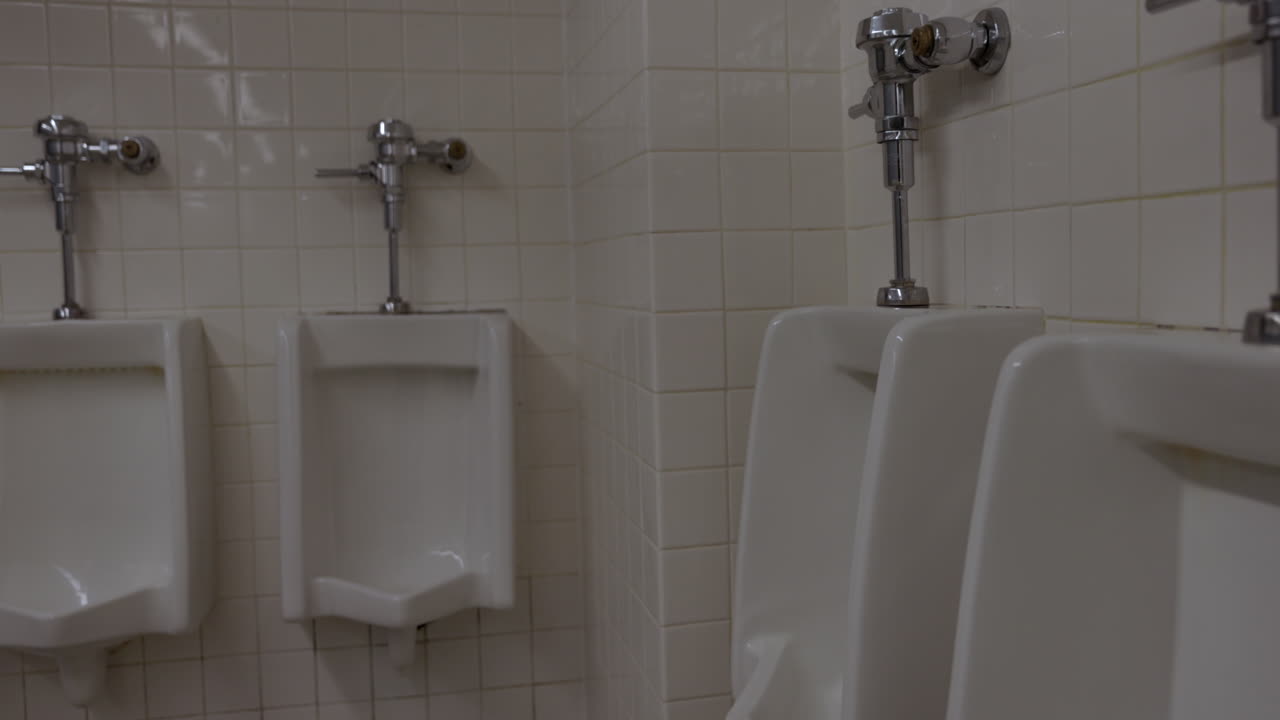 Urinals in public rest room bathroom - close up against white tile walls