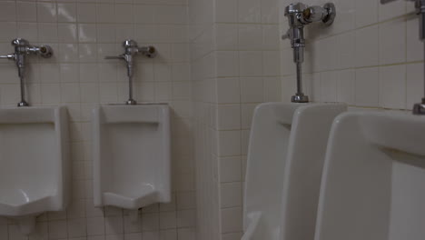 Urinals-in-public-rest-room-bathroom---close-up-against-white-tile-walls