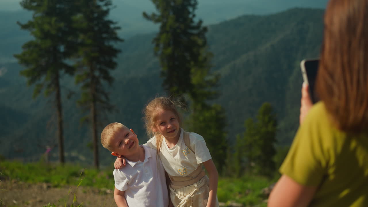 мать фотографирует позитивных детей на смартфоне на фоне холмистых гор дикой природы в туристической зоне. расслабляется с семьей и проводит время вместе в медленном движении