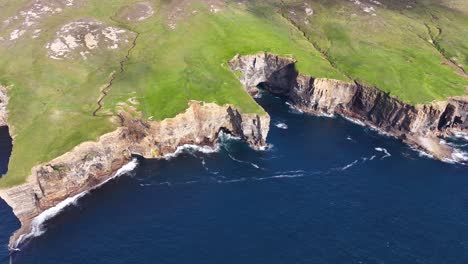 aerial view of steep cliffs above sea and green pastures on coastline of scotland uk