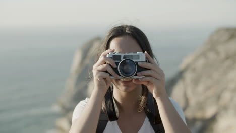 Front-view-of-a-young-dark-haired-girl-taking-photo-in-mountains